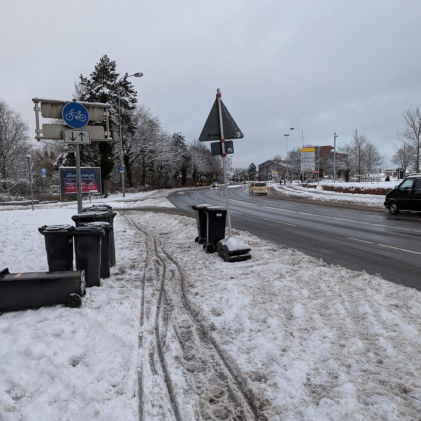 Eine geräumte Fahrbahn, nebenan ein Fahrradweg mit Schneematsch und Mülltonnen