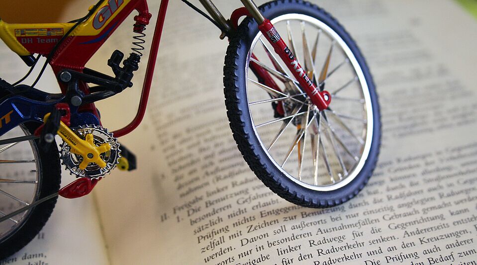 Deutscher Gesetzestext mit Fahrradbezug Miniatur-Fahrrad steht auf einem aufgeschlagenen Buch mit deutschem Gesetzestext.